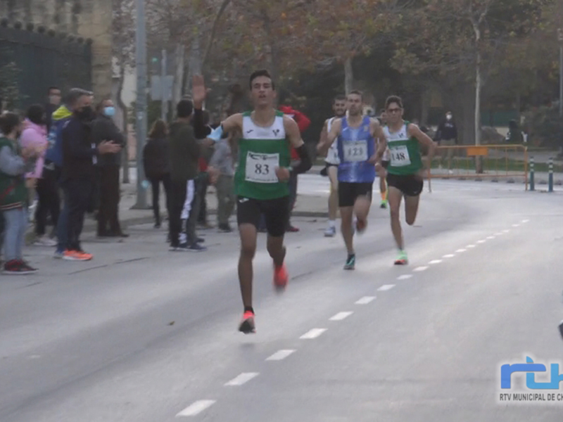 Corredores en una carrera de atletismo urbana, con participantes y espectadores en el fondo.