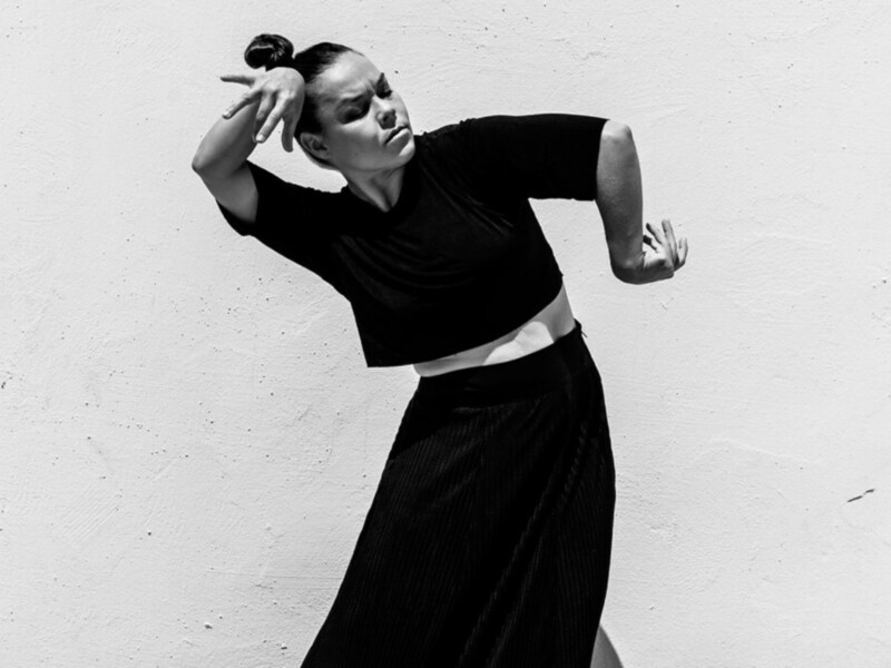 Dancer in motion against a plain wall, captured in black and white.
