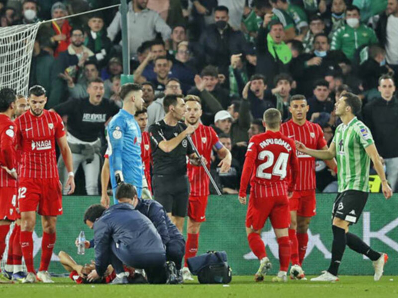 Un momento de tensión en un partido de fútbol, donde un jugador del equipo rojo está siendo ayudado por un médico mientras los jugadores del equipo verde observan la escena.