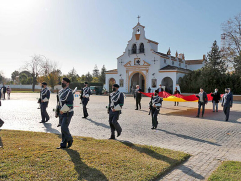 Desfile militar frente a una iglesia en Sevilla, España, con bandera española y uniformes tradicionales.