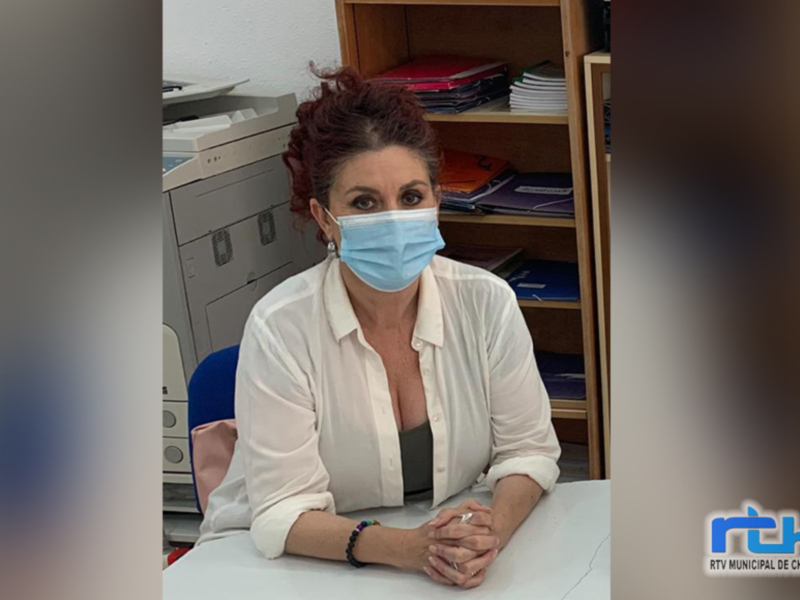 Mujer con mascarilla médica en un entorno de oficina, sentada con los brazos cruzados sobre una mesa.