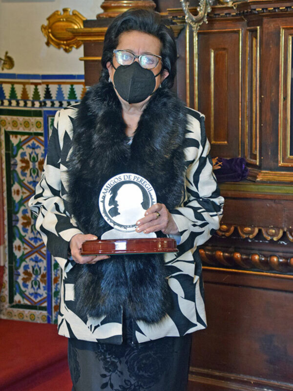 Persona con máscara y abrigo de piel posando con un trofeo en un entorno elegante.