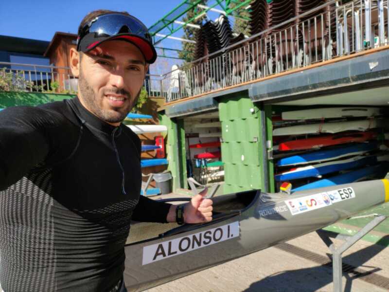 Retrato de un atleta de piragüismo frente a su balsa, con el nombre 'ALONSO I.' visible en la balsa.