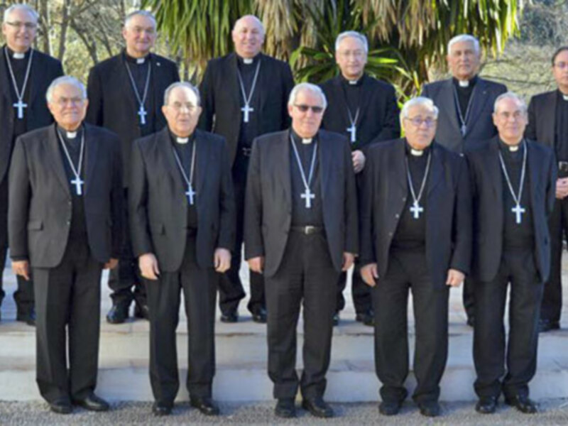 Un grupo de sacerdotes en trajes negros con cruces, posando al aire libre en un entorno verde.