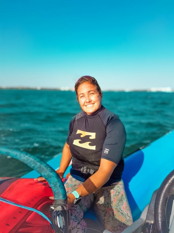 Una persona sonríe mientras navega en un catamarán en el mar, disfrutando del sol y el viento.