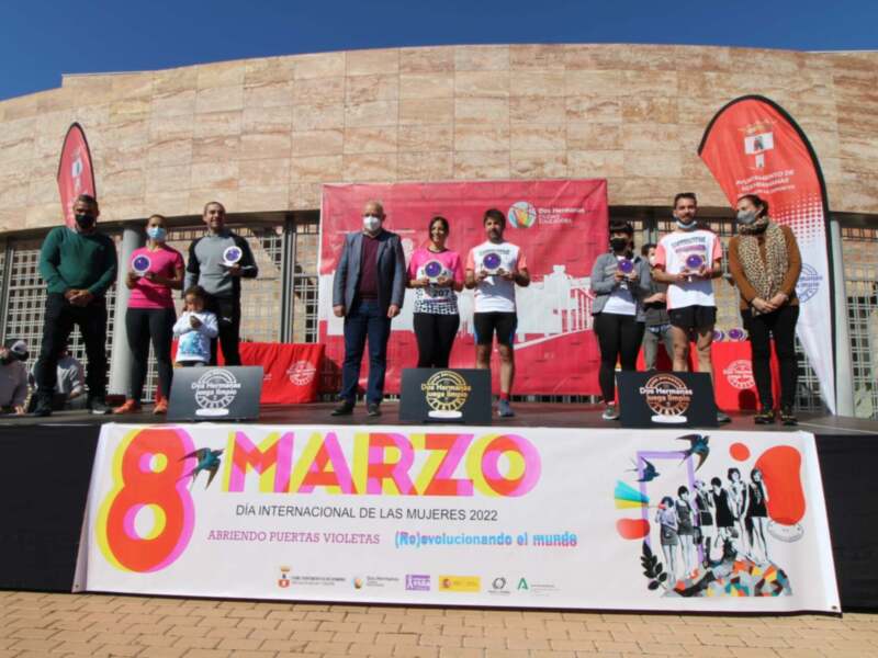 8 de Marzo, Día Internacional de las Mujeres 2022, celebración en Dos Hermanas, con corredores en el podio y un gran cartel promocionando la igualdad de género.