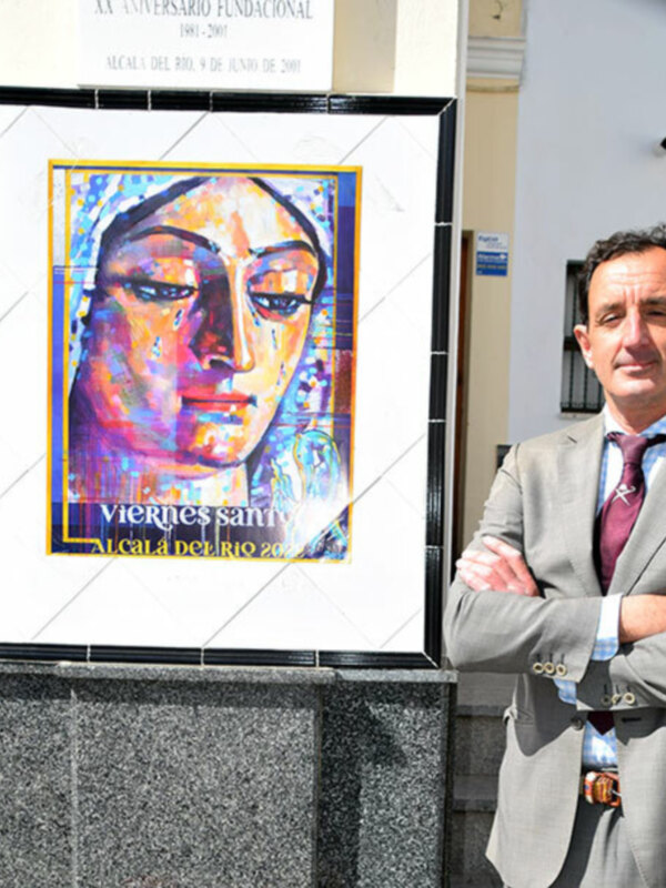 Un hombre en traje posa junto a una obra de arte que representa a una mujer con un fondo colorido y abstracto.