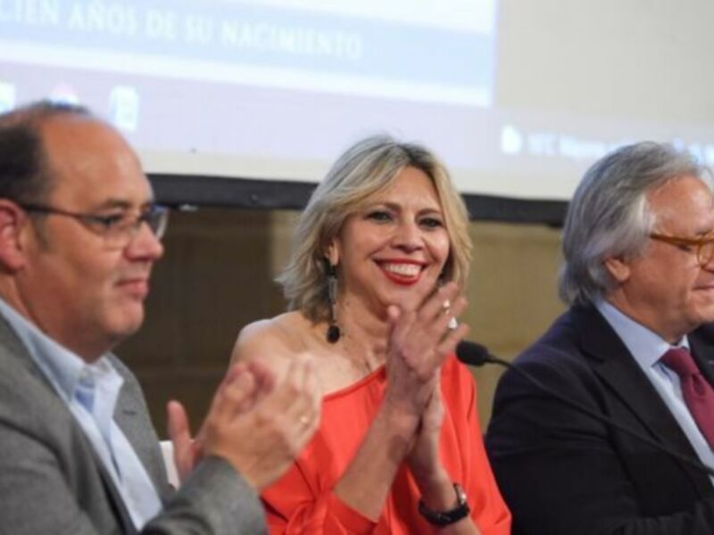 Una mujer sonriendo y aplaudiendo junto a dos hombres en un evento formal.