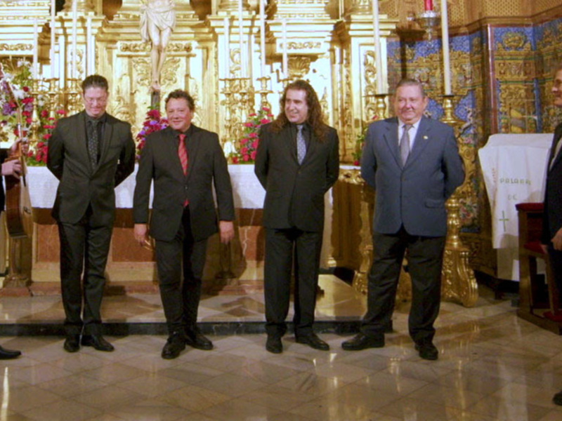 Cinco hombres en trajes formales posan frente a un altar ornamental en una iglesia.