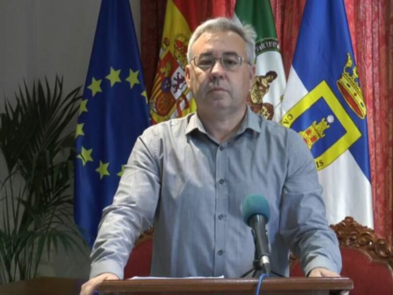 Persona hablando en rueda de prensa con banderas de la UE y España al fondo.