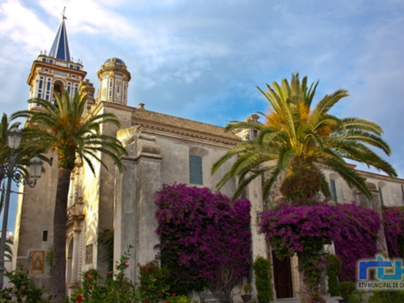 Iglesia histórica con cúpulas azules y palmeras en Chipiona, España.