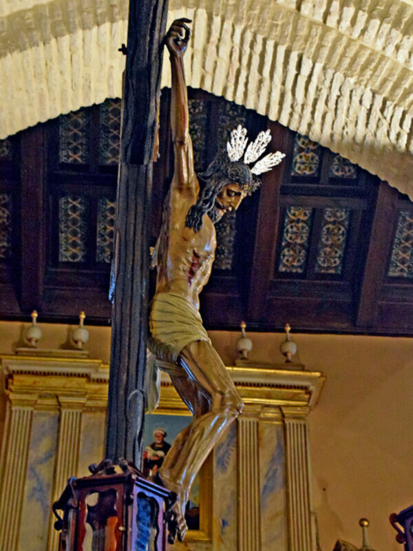 Estatua de Cristo crucificado en una iglesia, con detalles de la arquitectura y la iluminación.
