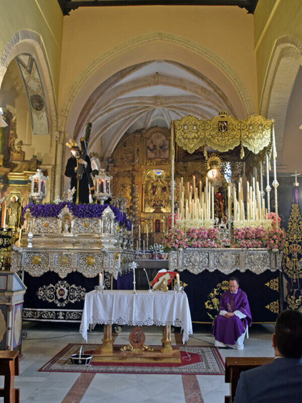 Interior de una iglesia con altares ornamentados y un sacerdote en el altar principal.