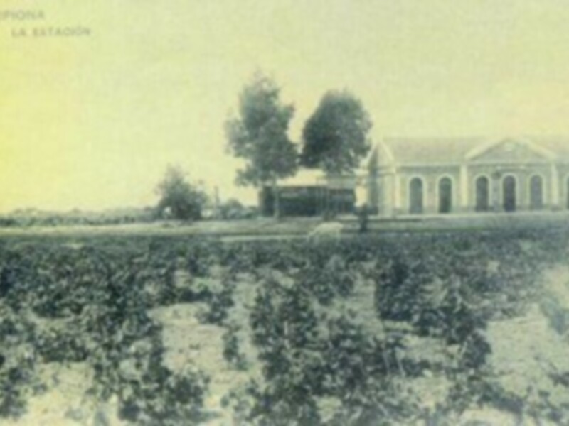 Imagen antigua de una estación ferroviaria con campos alrededor, en un estilo de grabado o tinta negra.