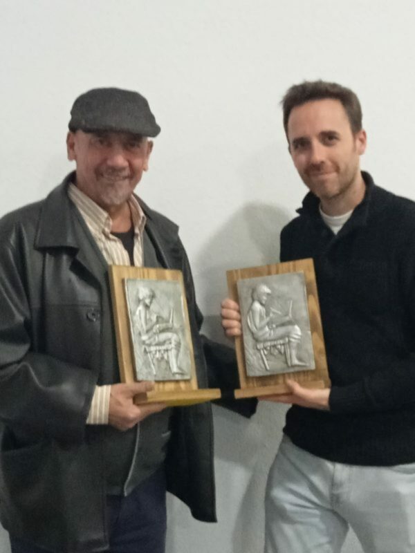 Dos personas posan con placas de reconocimiento en un evento formal.