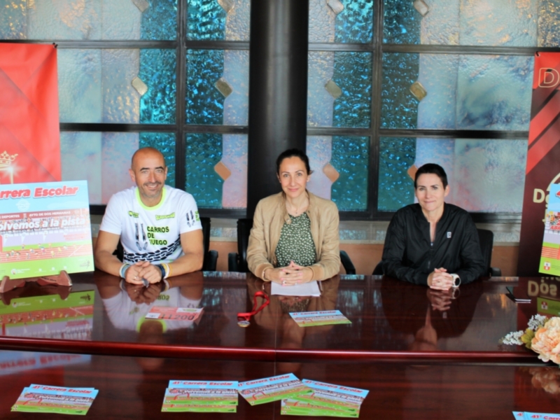 Presentación de la Carrera Escolar en la sala de prensa municipal, con tres personas sentadas en una mesa y carteles promocionales en el fondo.
