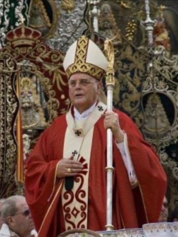 Un sacerdote en traje rojo y manto blanco sostiene un bastón de plata, participando en una ceremonia religiosa.