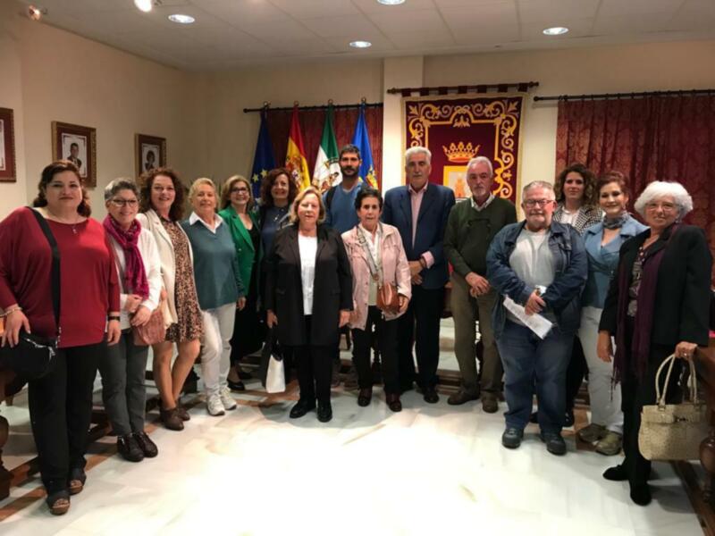 Una reunión formal de personas en un salón con banderas y un escudo de armas en el fondo.