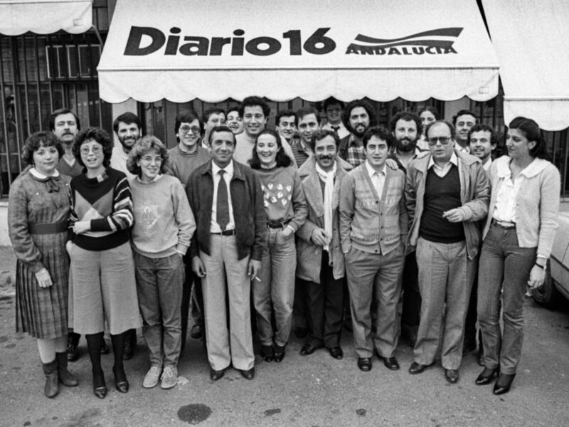 Equipo de trabajo en una oficina, con una persona en el centro que sostiene una galleta con el nombre 'Diario'.