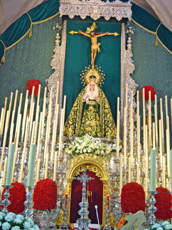 Altar con Virgen María en trono dorado, rodeada de candelabros y flores, en un ambiente religioso y festivo.