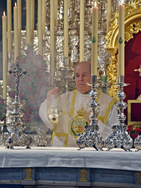 Un sacerdote realiza una ceremonia religiosa con incienso y velas en un altar ornamental.