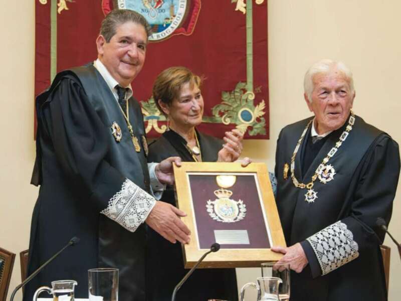 Un hombre en traje de gala sostiene un diploma mientras una mujer y otro hombre lo miran.