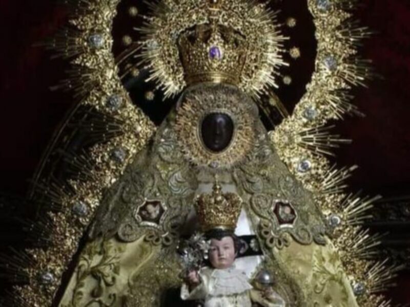 Imagen de la Virgen María con el Niño Jesús, vestida con una túnica dorada y un halo de diamantes, en una iglesia. La imagen muestra la majestuosidad y la devoción hacia la Virgen María en la cultura católica.