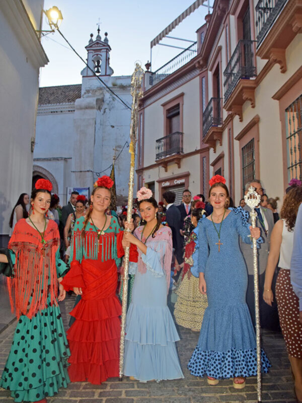 Desfile de mujeres vestidas con trajes típicos flamencos en una calle de pueblo español.
