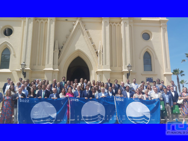 Gruppo di persone in abiti formali con una bandiera blu che dice '2022' davanti a una chiesa con archi gotici.