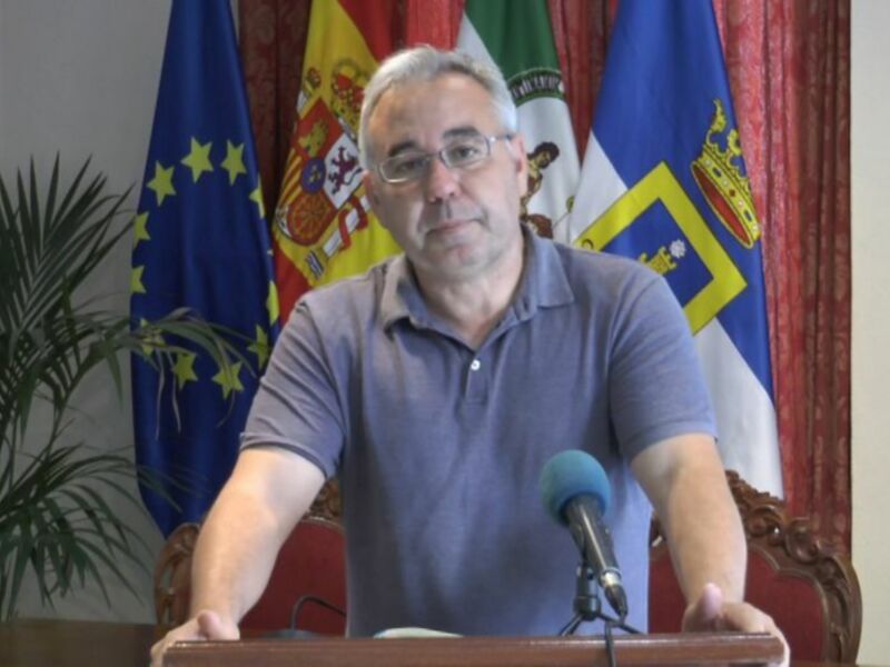 Un hombre se dirige a la audiencia en una conferencia de prensa, con banderas de España y la Comunidad de Madrid en el fondo.