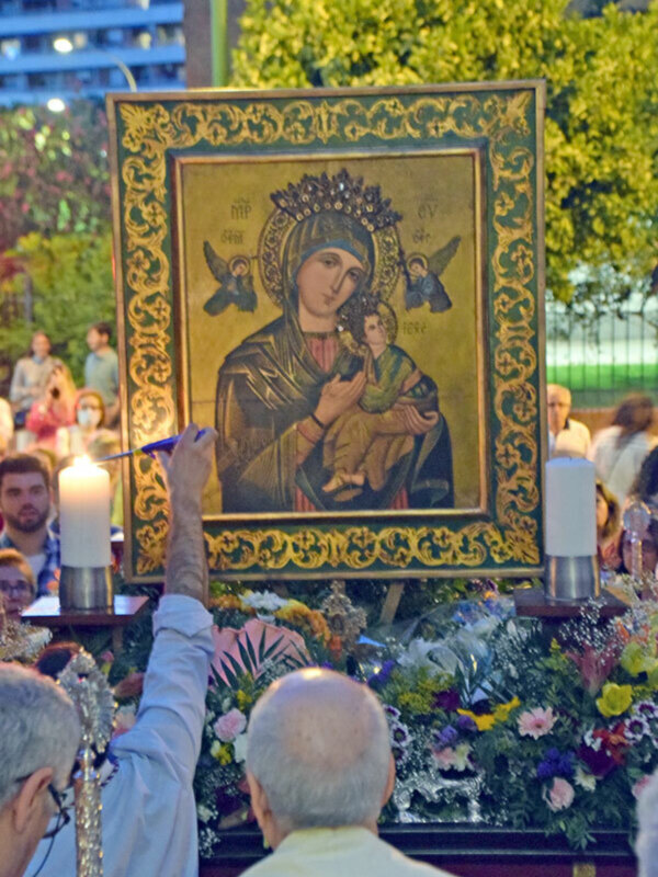 Procesión religiosa con icono de la Virgen María y Niño Jesús, rodeado de flores y velas iluminadas.