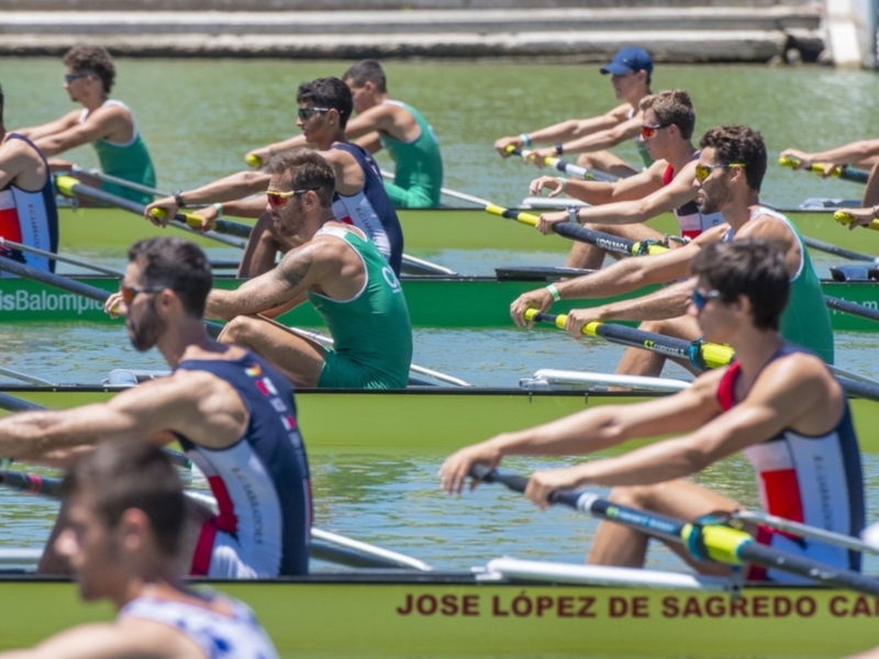 Equipo de remo en competencia en un canal bajo el sol brillante.