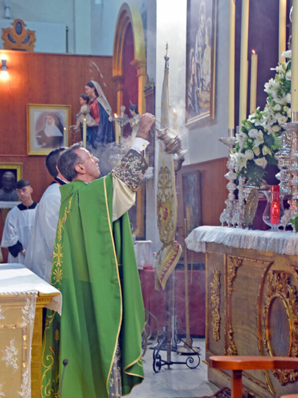 Un sacerdote realiza una bendición con incienso en una iglesia decorada con altares y estatuas religiosas.