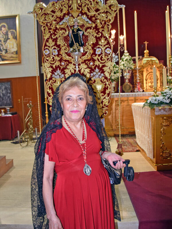 Mujer vestida con traje tradicional español en una iglesia, con un fondo ornamental dorado y rojo.