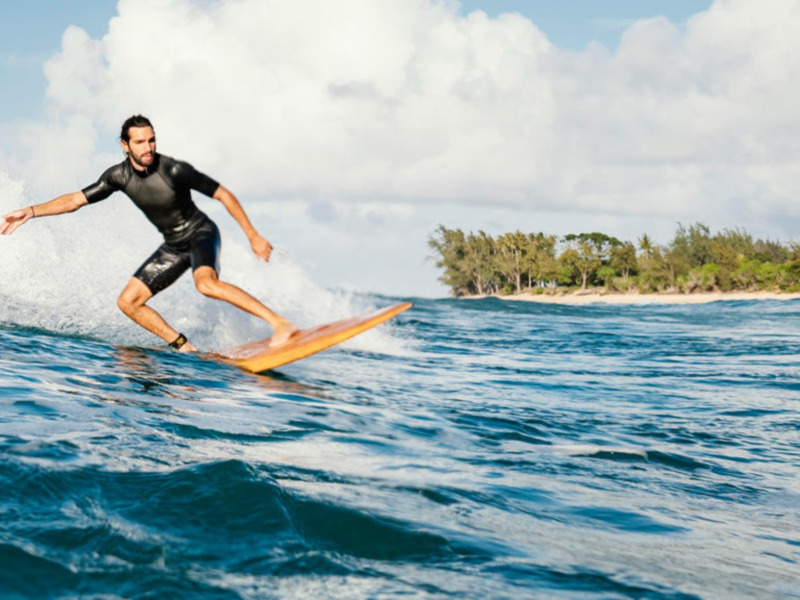 Surfer en acción en una ola, con un paisaje tropical en el fondo.