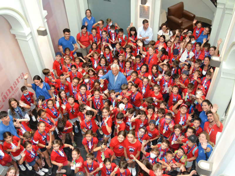 Un grupo de niños y adultos celebrando juntos, todos vestidos con camisetas rojas y medallas, en un ambiente formal y acogedor.