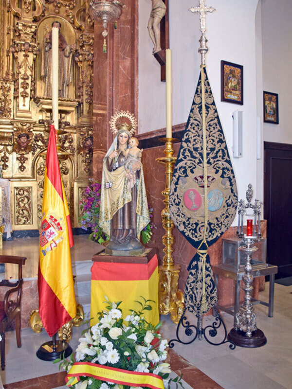 Estatua de la Virgen con el Niño en un altar con bandera española y ornamentos religiosos.