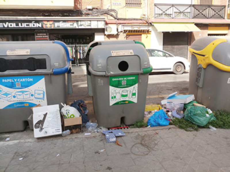 Contenedores de reciclaje y basura en la acera de una calle urbana.