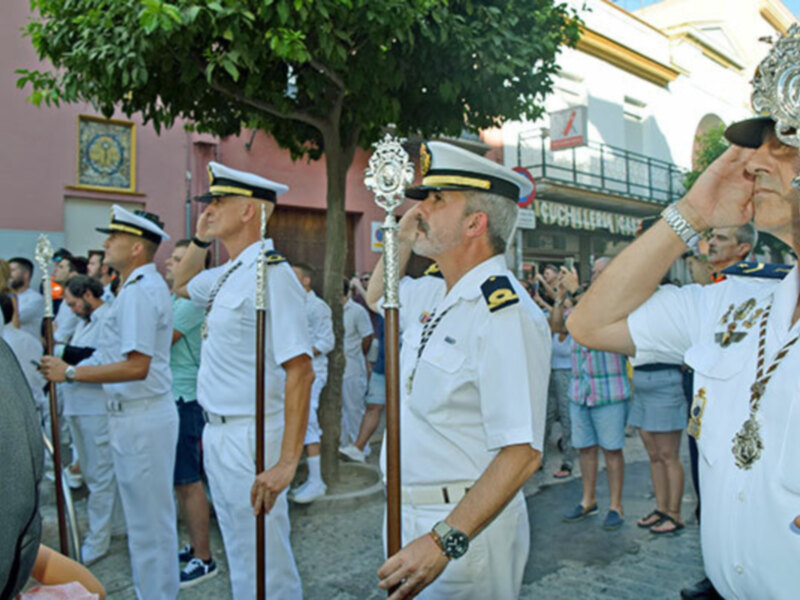 Oficiales en uniforme blanco participando en una procesión en una calle urbana.