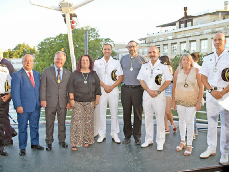 Grupo de personas en uniforme naval y civiles posando en un evento al aire libre.