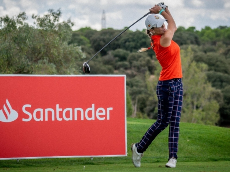 Jugador de golf en acción con cartel de Santander en el fondo.