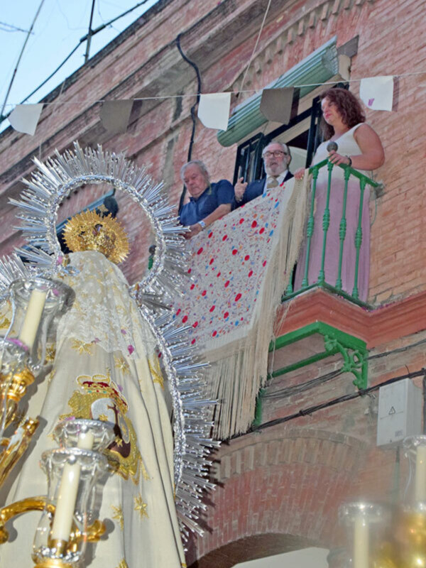 Procesión religiosa con imagen de la Virgen y personas en un balcón observando.