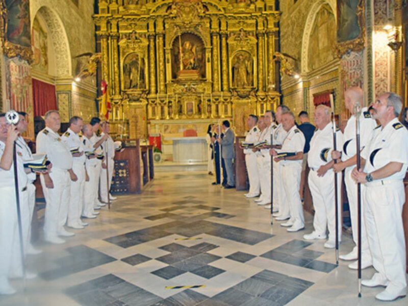 Fotografía de oficiales militares en uniforme blanco, posando en una iglesia con detalles dorados y vitrales, con una cruz en el suelo.