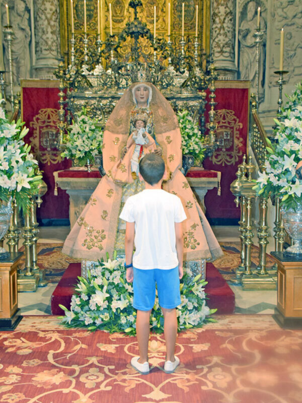 Un niño frente a una imagen religiosa en una iglesia, rodeado de flores y decoraciones.