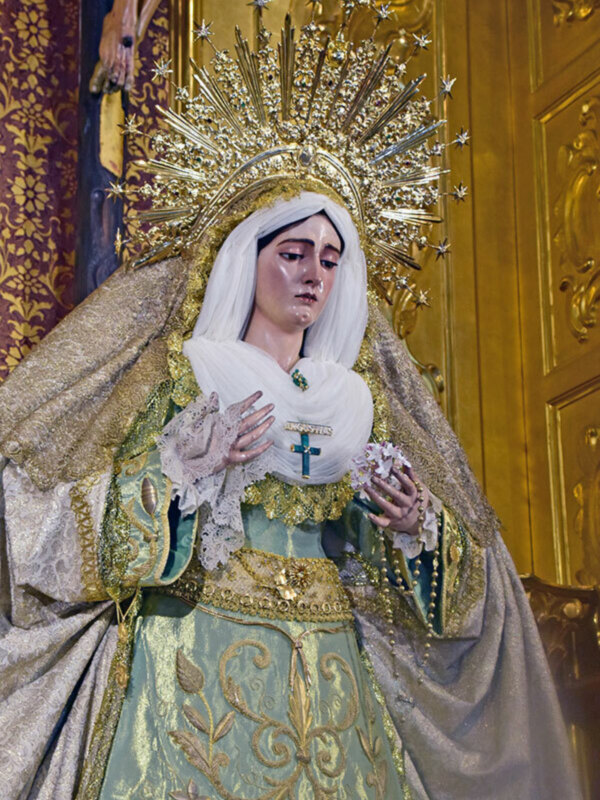 Estatua de la Virgen María con una aureola dorada y vestimentas ornamentadas en un entorno eclesiástico.