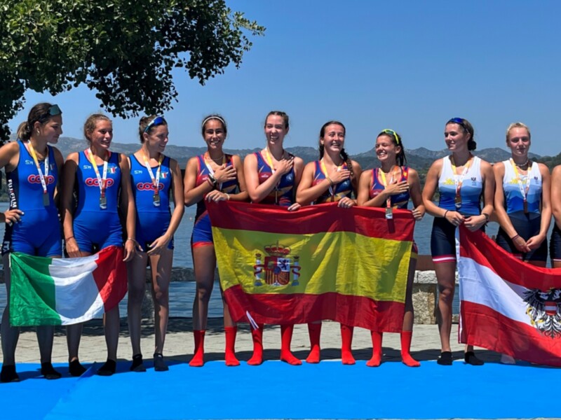 Equipo de remo femenino celebrando con banderas y medallas tras una competición.