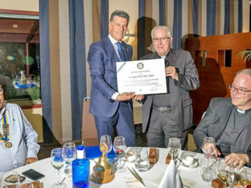 Entrega de reconocimiento en una cena formal, con individuos en trajes y un certificado en mano.