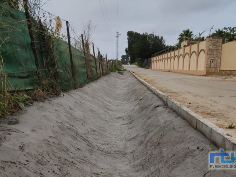 Vista de una carretera con una cerca de contención de arena en el lado izquierdo, y una pared de piedra en el lado derecho. El cielo es nublado.
