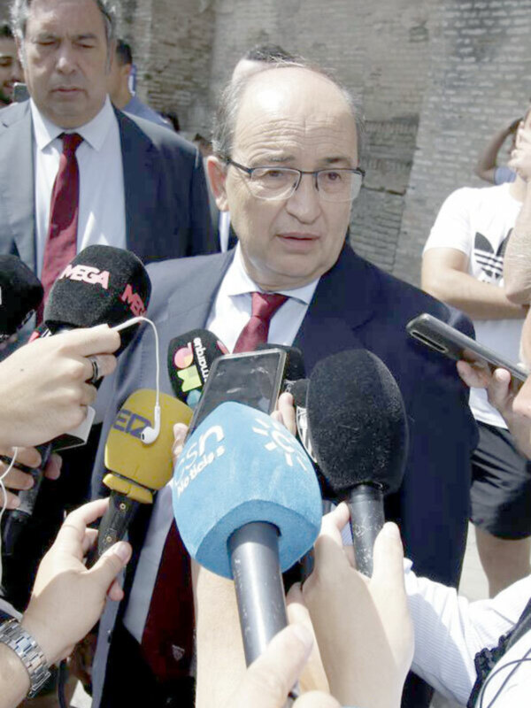 Un hombre en traje hablando con micrófonos de diferentes medios de comunicación en una entrevista.