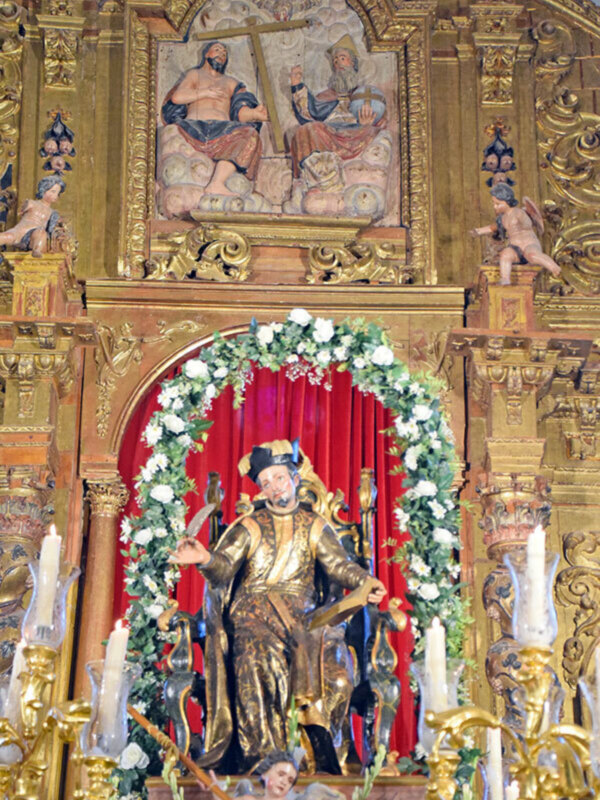 Altar de una iglesia con estatua dorada, flores y velas.